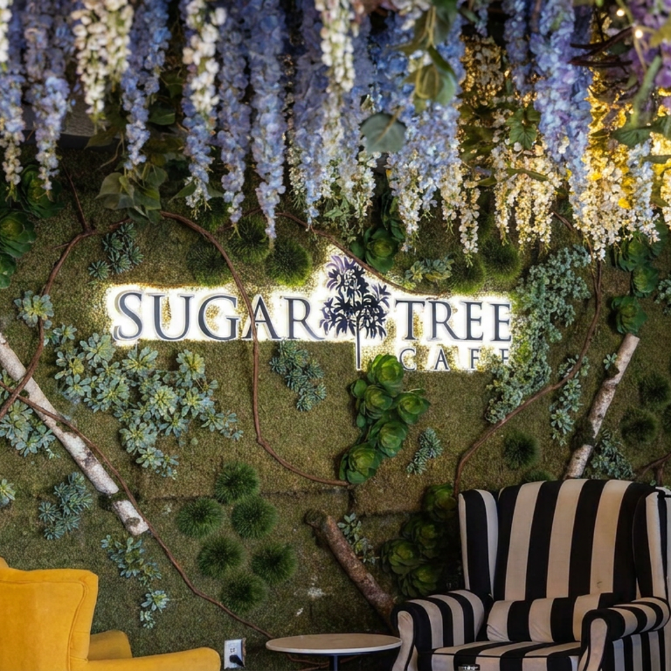 Sugar Tree Cafe sign on a lush moss wall with hanging flowers, succulents, decorative branches, and colorful lounge chairs.